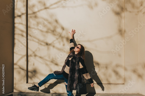 Beautiful brunette young woman in nice brown, yellowish wall, in sweater with stripes, jeans and sunglasses. Fashion spring photo. outdoors photo