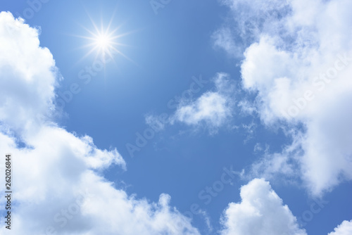 Sun on blue sky with white clouds.