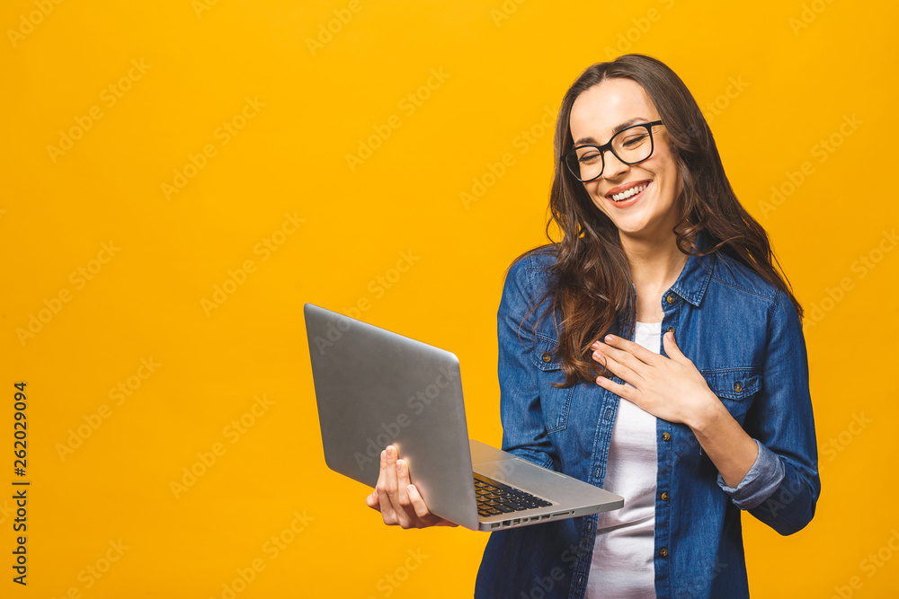 Φωτογραφία Young happy smiling woman in casual clothes holding laptop and sending email to her best friend isolated against yellow background