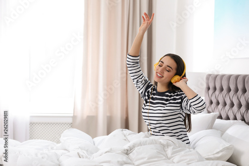 Young woman with headphones enjoying music in bed