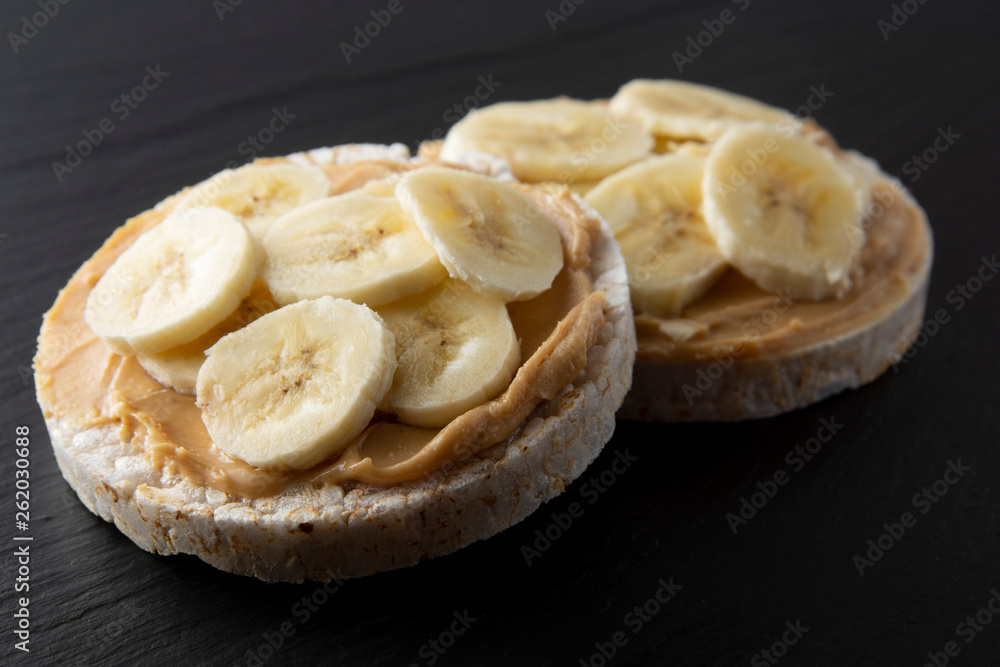 Peanut butter and banana on rice cakes, healthy, dietary food. Black background.