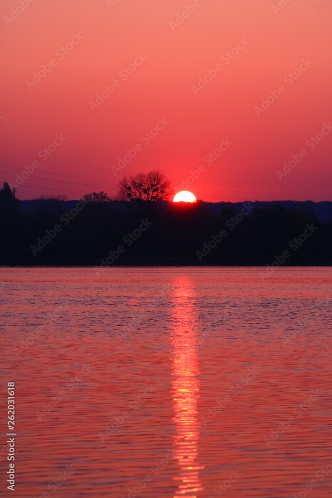 Naklejka premium Wonderful and romantic sunrise. Half of rising sun on the horizon with its golden reflections in the water