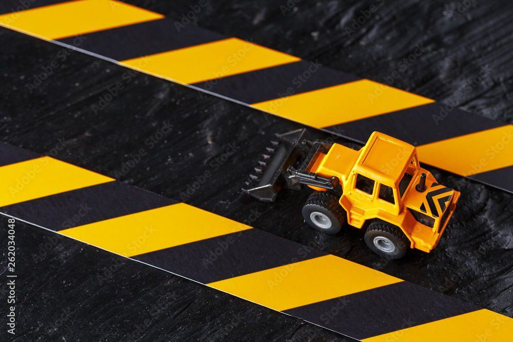 Naklejka premium Yellow toy bulldozer on a black background texture. Black and yellow fence tape against the background of the CONCEPT