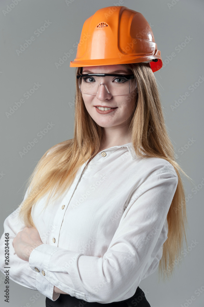 Portrait of a young attractive woman with blond hair in orange helmet on a neutral gray background. Portrait of a young attractive woman with blond hair in orange helmet on a neutral gray background.