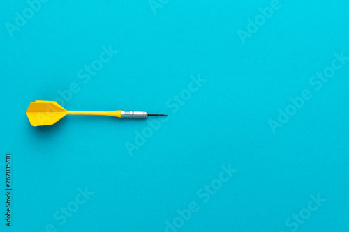 minimalist photo of yellow plastic dart with metal tip on blue background