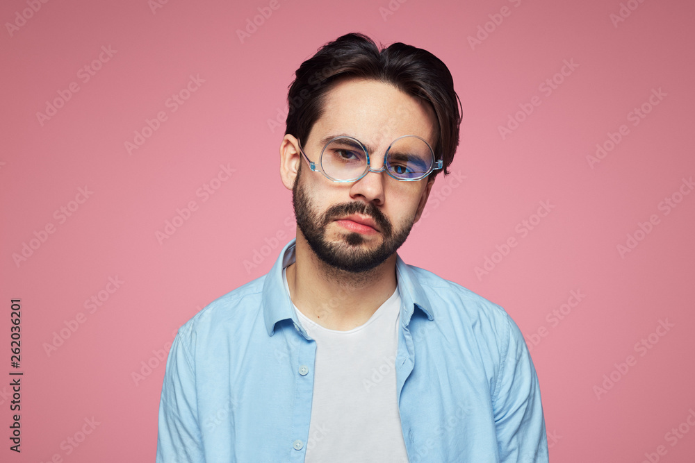 Obraz premium Stylish unshaven guy with bored fed up expression, tired after a long hard working day, isolated over pink background