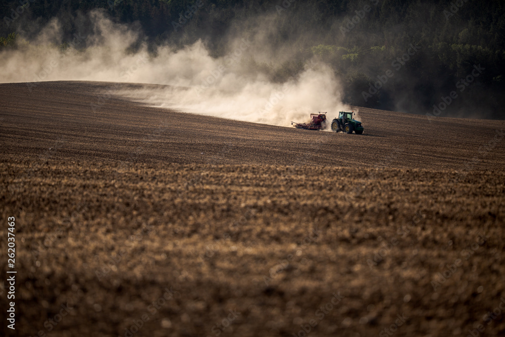 Tractor plowing a dry farm field - acute drought the soil suffers from being quite obvious from the amount of dust Tractor plowing a dry farm field - acute drought the soil suffers from being quite obvious from the amount of dust