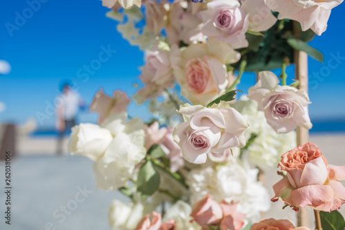 Fototapeta Naklejka Na Ścianę i Meble -  Part of the wedding arch decorated with fresh flowers is set on the sandy bank of the river. Wedding florist arranges workflow