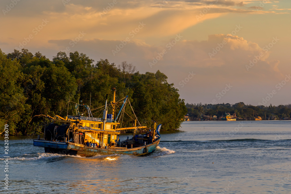 Fishing boat moves on the river against the backdrop of a tropical forest  at sunset Stock Photo