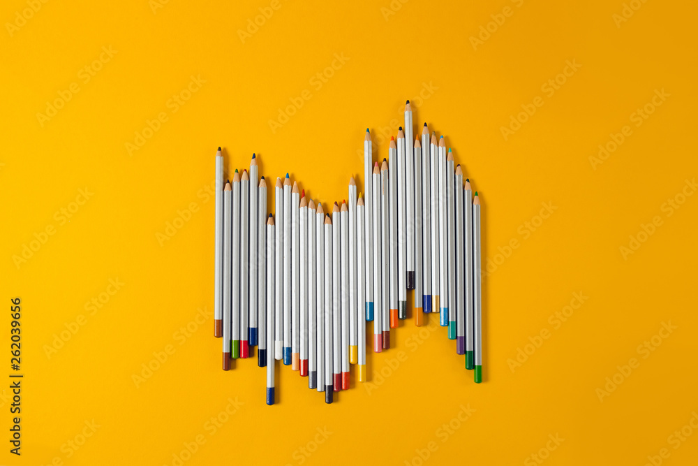 colored pencils arranged in a chaotic line on yellow background colored pencils arranged in a chaotic line on yellow background