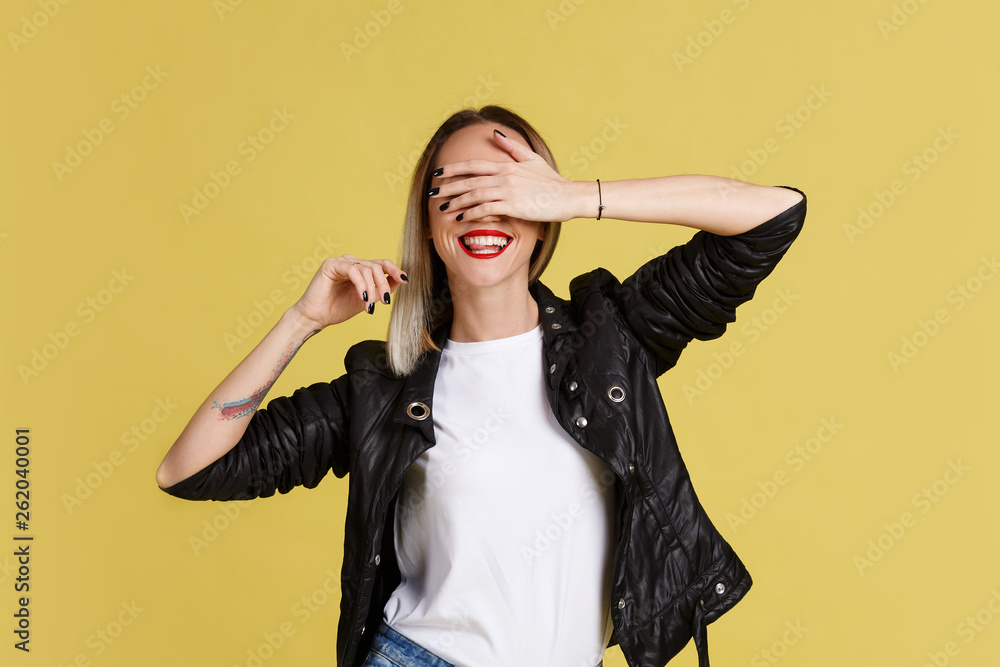 Portrait of young smiling woman with red lips covered eyes to see surprise. Funny excited girl with ombre and black leather jacket on yellow background. Portrait of young smiling woman with red lips covered eyes to see surprise. Funny excited girl with ombre and black leather jacket on yellow background.