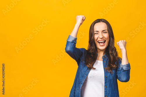 I'm winner! Happy successful young woman with raised hands shouting and celebrating success over yellow background. photo