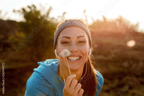 Beautiful athletic woman holding dandelion and looking at camera.