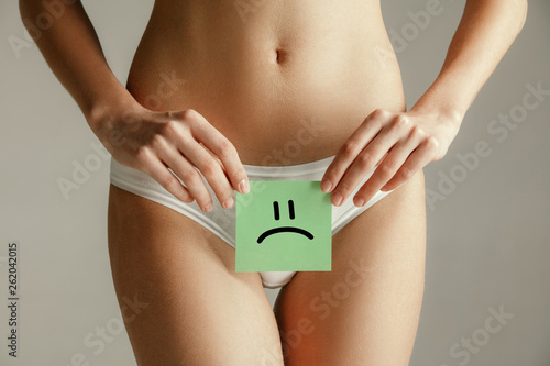 Woman health. Female model holding card near stomach. Young adult girl with paper for symbol on gray studio background. Negative emoji as sign of problems. Medical problem and solution.