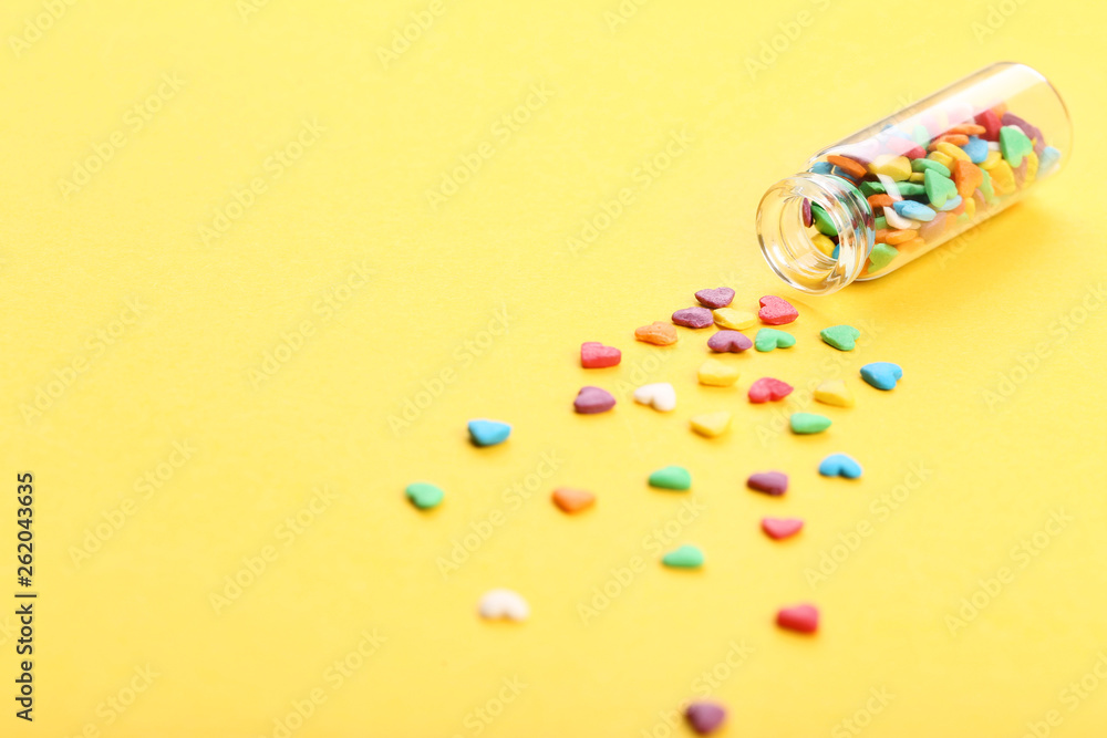 Colorful heart shaped sprinkles in glass bottle on yellow background Colorful heart shaped sprinkles in glass bottle on yellow background