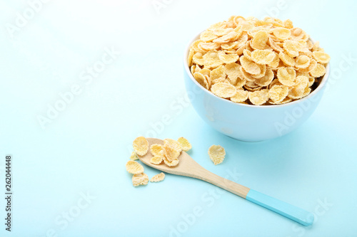 Corn flakes in bowl with spoon on blue background
