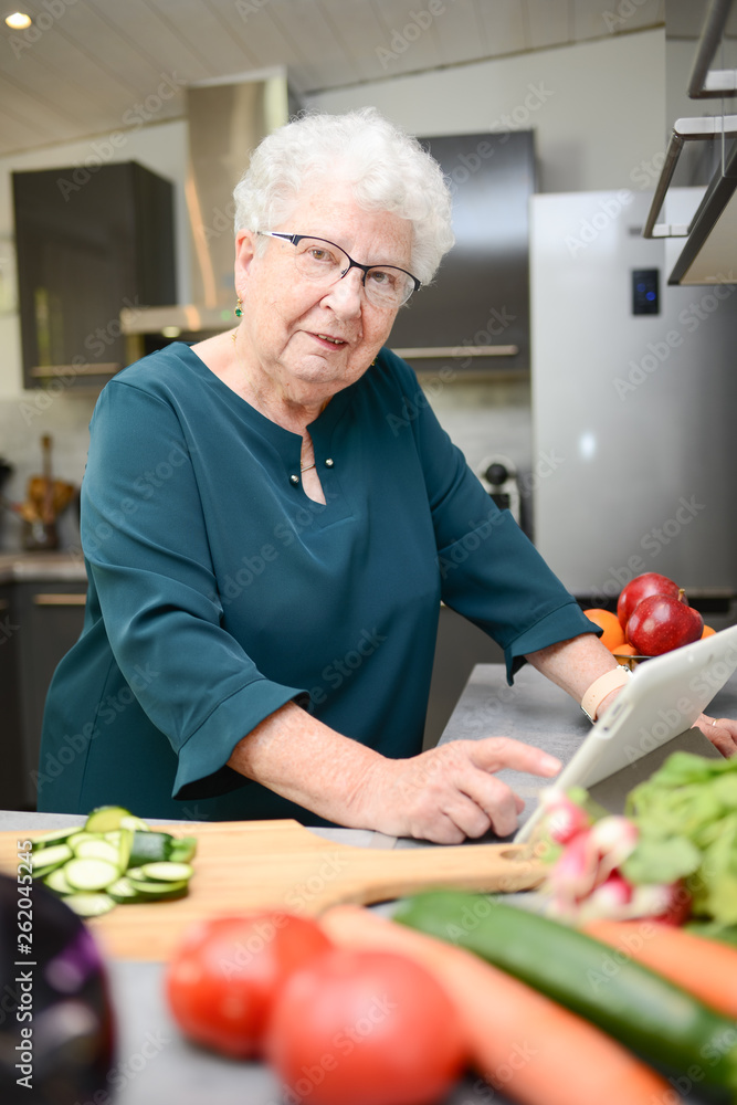 happy senior active woman cooking at home in modern kitchen and looking for recipe on a internet computer tablet happy senior active woman cooking at home in modern kitchen and looking for recipe on a internet computer tablet