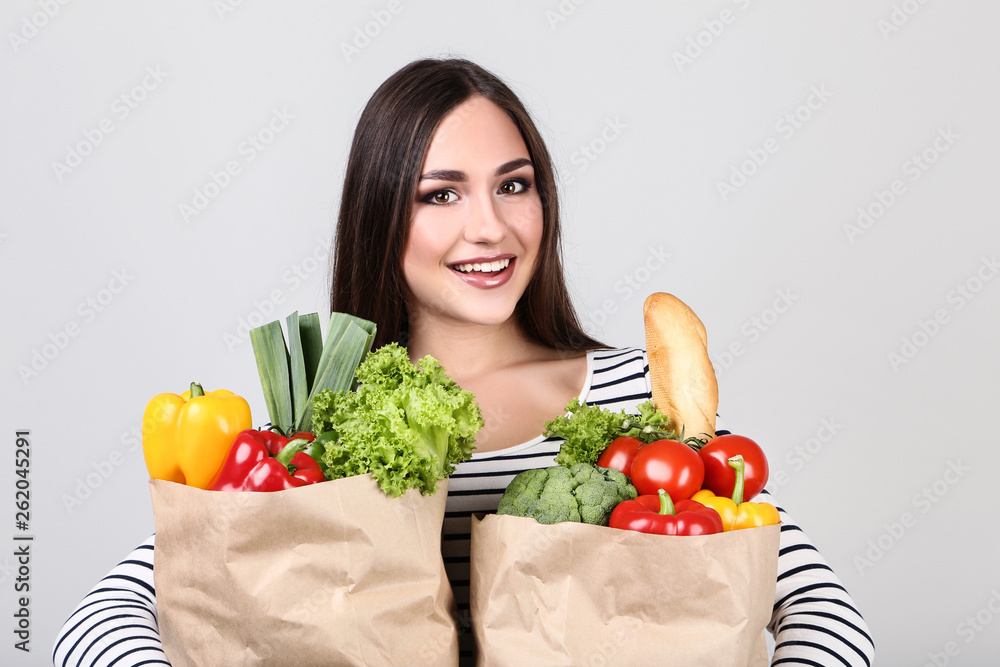 Beautiful woman holding grocery shopping bags on grey background Beautiful woman holding grocery shopping bags on grey background