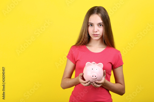 Young girl holding pink piggybank on yellow background
