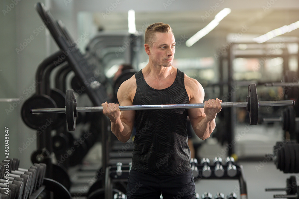 handsome man in good physical condition with muscles in the gym training with barbell handsome man in good physical condition with muscles in the gym training with barbell