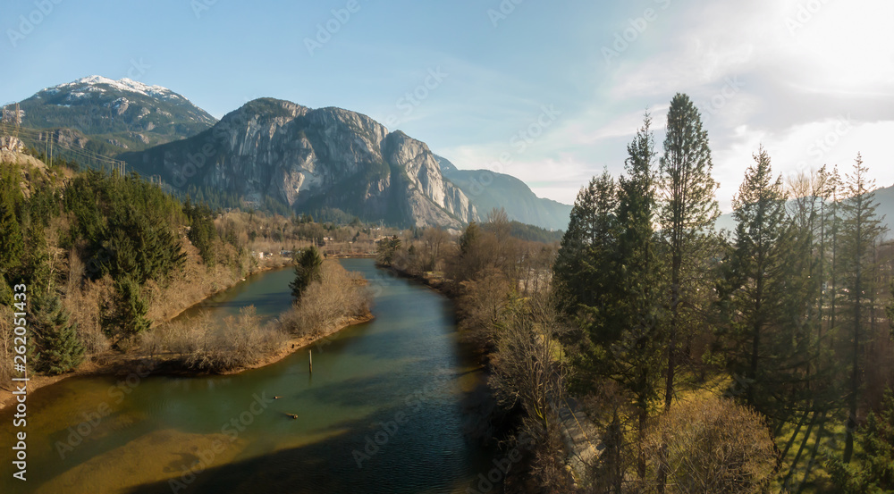 Aerial panoramic view of a small town with Chief Mountain in the background during a sunny day. Taken in Squamish, North of Vancouver, British Columbia, Canada.