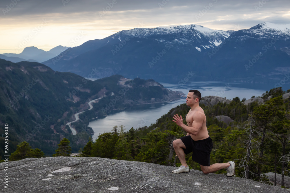 Fit and Muscular Young Man is doing exercises on top of the Mountain during a cloudy sunset. Taken on Chief Mountain in Squamish, North of Vancouver, BC, Canada.