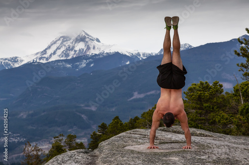 Obraz na plátně Fit and Muscular Young Man is doing exercises on top of the Mountain during a cloudy day