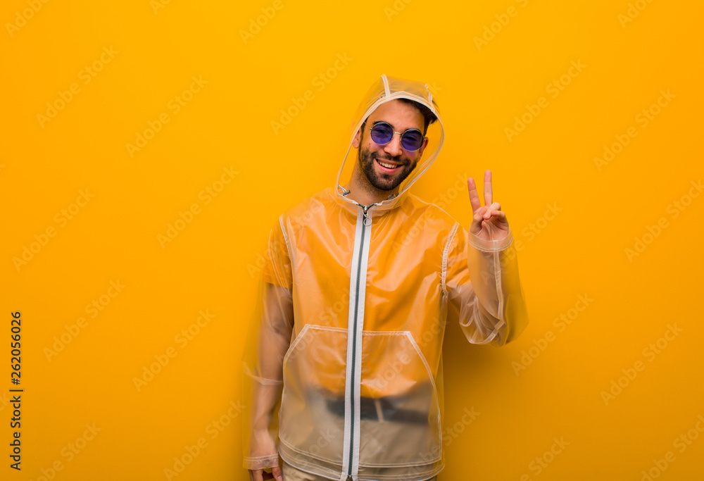 Young man wearing a rain coat doing a gesture of victory Young man wearing a rain coat doing a gesture of victory