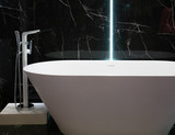 modern white bathtub at hotel apartment with black marble wall on background. contemporary interior design at bathroom