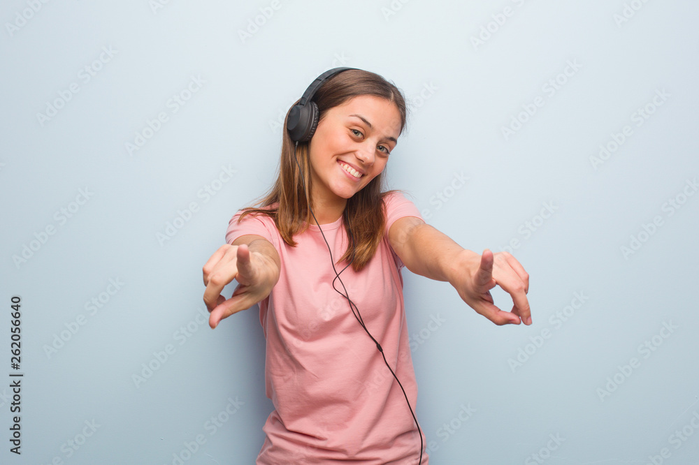 Young pretty caucasian woman cheerful and smiling pointing to front. She is listening to music with headphones. Young pretty caucasian woman cheerful and smiling pointing to front. She is listening to music with headphones.