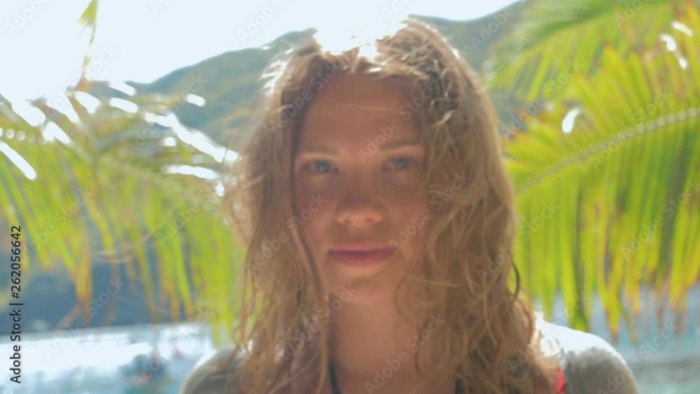 Slow motion close-up gimbal shot of beautiful european young woman on tropical beach looking in the camera Slow motion close-up gimbal shot of beautiful european young woman on tropical beach looking in the camera
