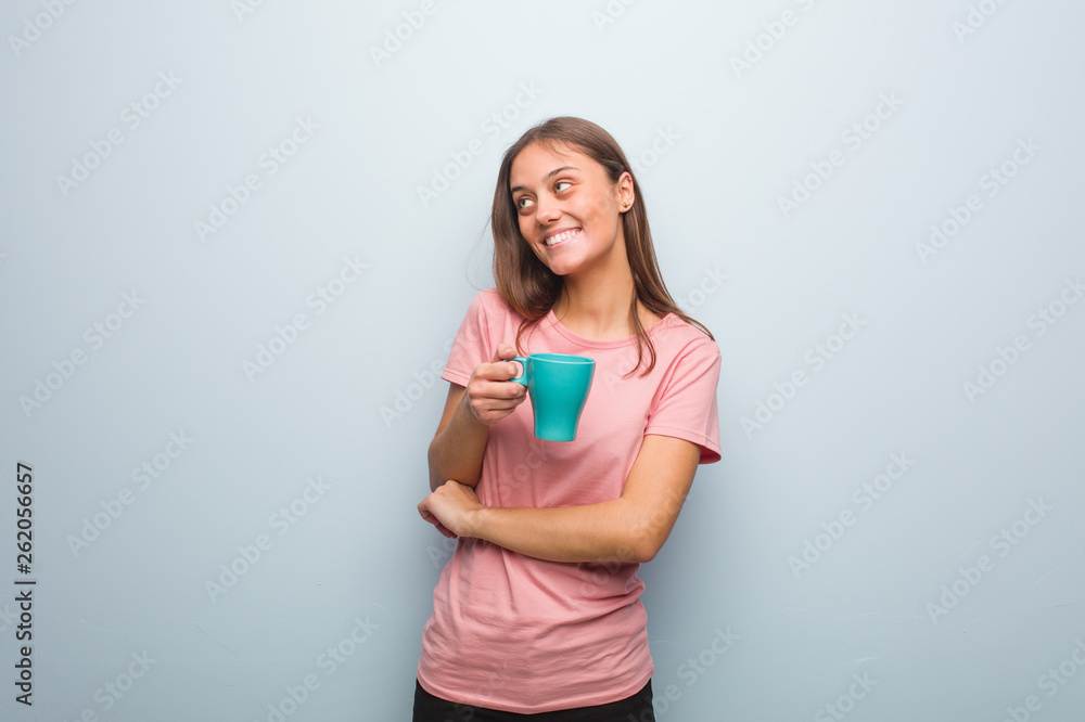 Young pretty caucasian woman smiling confident and crossing arms, looking up. She is holding a mug. Young pretty caucasian woman smiling confident and crossing arms, looking up. She is holding a mug.