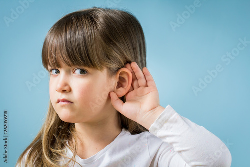 Toddler girl with hearing problem on light blue background. Close up, copy space.