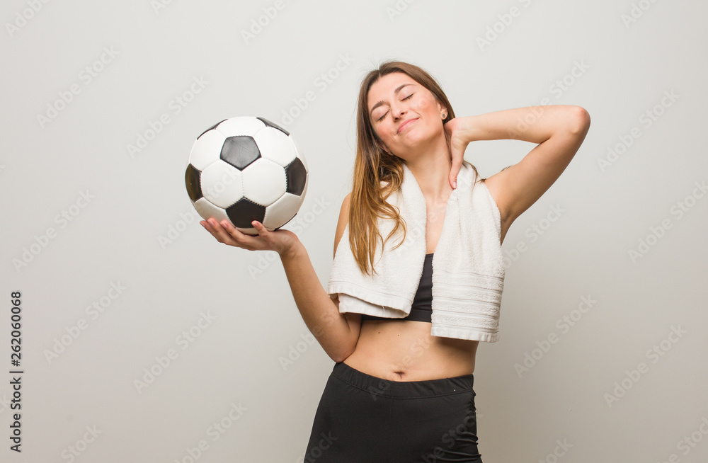 Young fitness russian woman suffering neck pain. Holding a soccer ball.