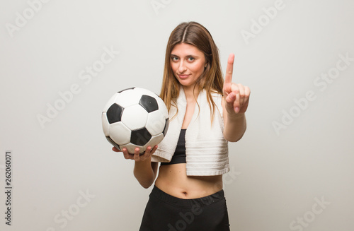 Young fitness russian woman showing number one. Holding a soccer ball.