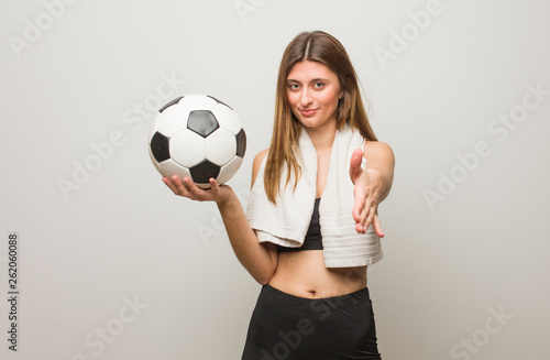 Young fitness russian woman reaching out to greet someone. Holding a soccer ball.