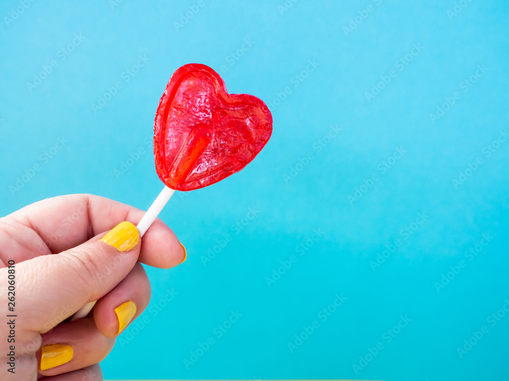 A woman with yellow painted nails with a red lollipop in her hand and blue background