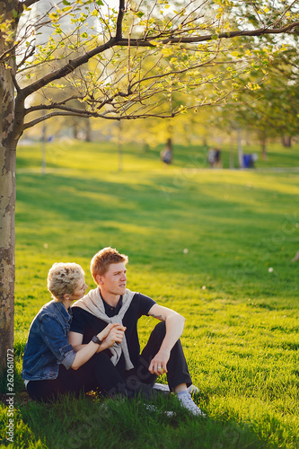 stylish and beautiful woman with short light hair, dressed in a blue jeans jacket sitting with her handsome man in a sunny green park © prostooleh