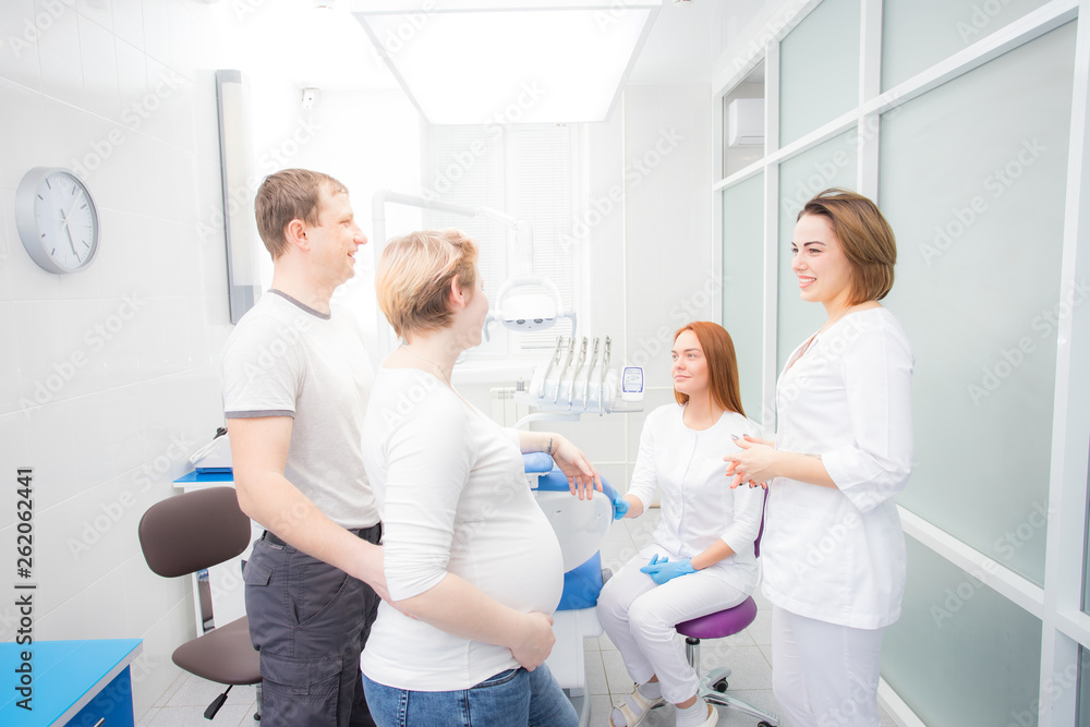 Fototapeta premium pregnant woman and her husband communicate with two young women dentists in a medical office. Dental treatment for pregnant women