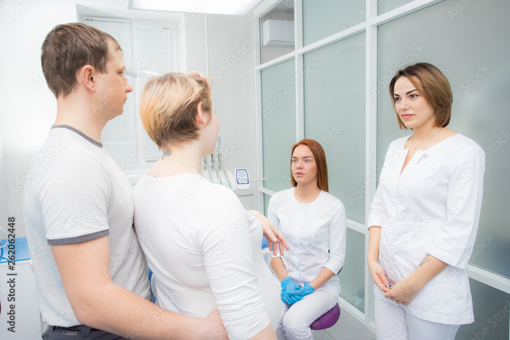 Obraz premium pregnant woman and her husband communicate with two young women dentists in a medical office. Dental treatment for pregnant women