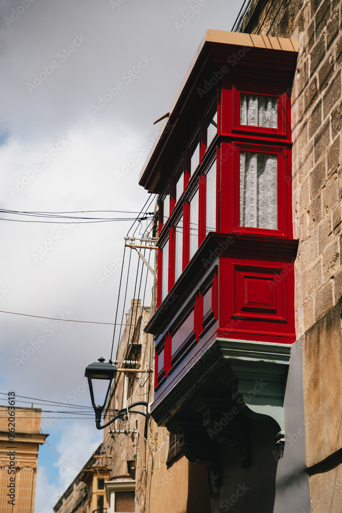 Typical traditional wooden red maltese balcony at narrow medieval street in Mdina, ancient capital of Malta, fortified medieval town. Popular touristic destination and attraction Typical traditional wooden red maltese balcony at narrow medieval street in Mdina, ancient capital of Malta, fortified medieval town. Popular touristic destination and attraction