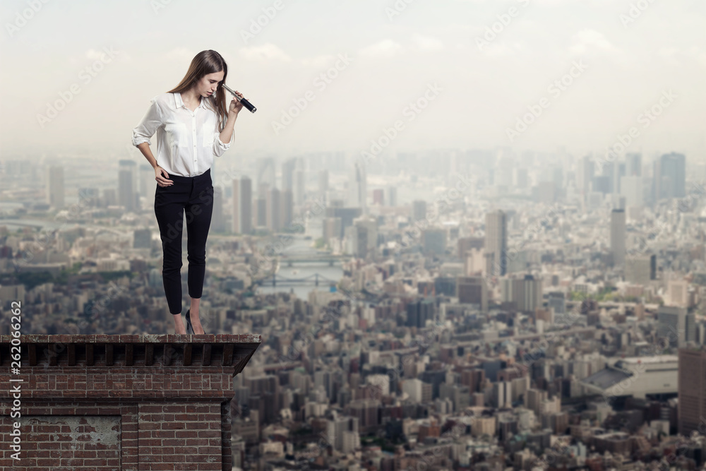 Beautiful woman on a roof top looking through a telescope at a city