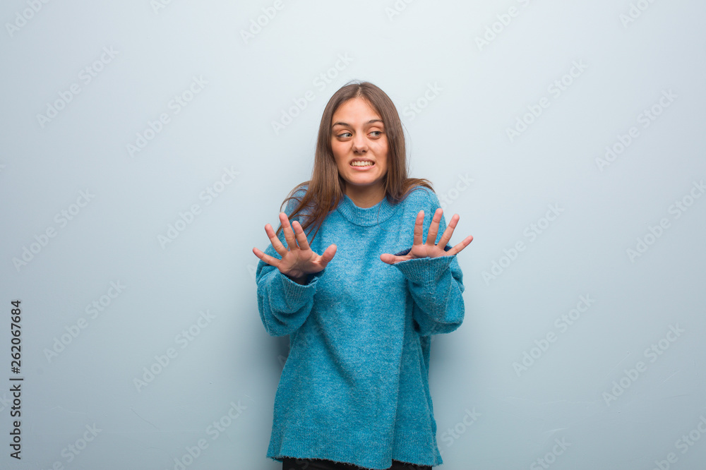 Young pretty woman wearing a blue sweater rejecting something doing a gesture of disgust Young pretty woman wearing a blue sweater rejecting something doing a gesture of disgust