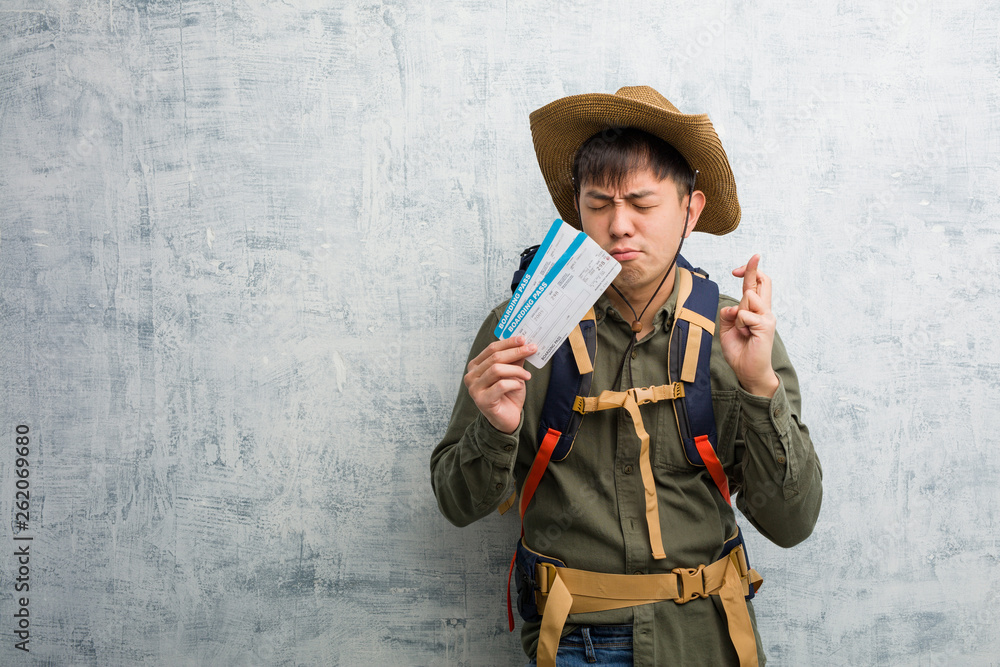Young explorer chinese man holding an air tickets crossing fingers for having luck Young explorer chinese man holding an air tickets crossing fingers for having luck