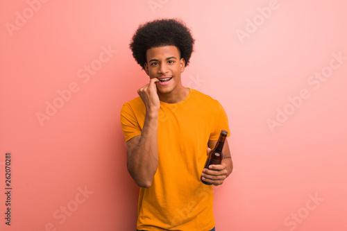 Young african american man holding a beer biting nails  nervous and very anxious