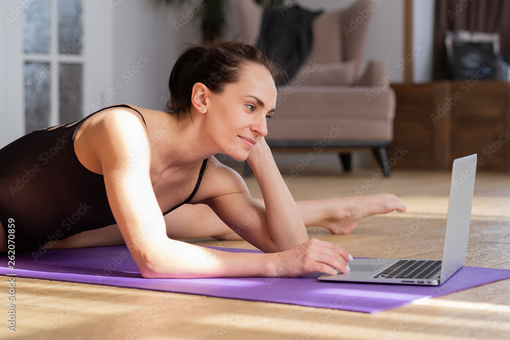 Charming young athlete with pleasure lies in the splits, working at the computer Charming young athlete with pleasure lies in the splits, working at the computer
