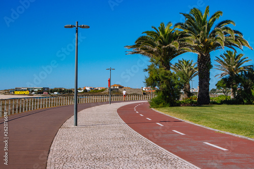 Esposende, Portugal - 10/03/2018: Empty road to beach with palms. Health path along seacoast. Travel and vacation concept. Empty street with palm trees. Sunny day in Portugal. Walkway near the ocean. photo