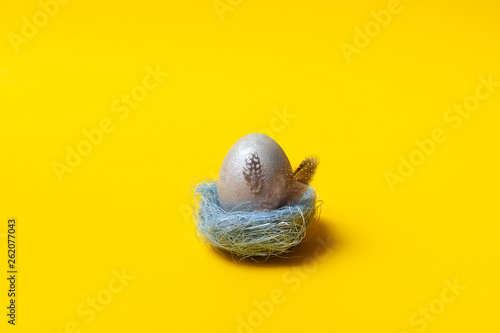 Easter, silver egg on yellow background. Decorated with feathers. 