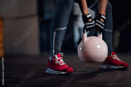 Unrecognizable sportswoman practicing with kettle bell in a gym.