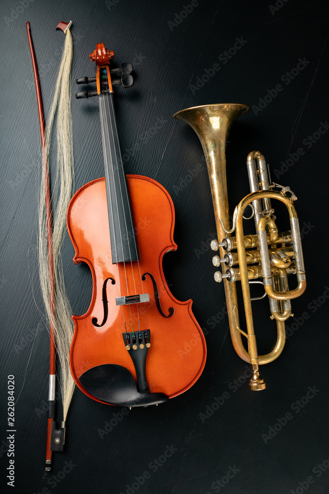 Naklejka premium A new shining violin and an old trumpet on a dark table. Musical instruments, stringed and wind.